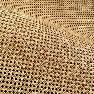 May include: Close-up of a woven rattan material with a repeating pattern of diamond-shaped openings. The natural tan color of the rattan creates a textured surface. The weave is dense, creating a sturdy and flexible material.