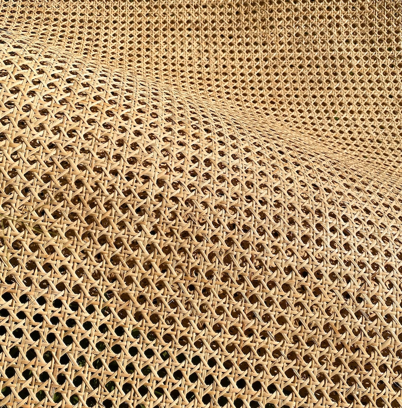 May include: Close-up of a woven rattan material with a repeating pattern of diamond-shaped openings. The natural tan color of the rattan creates a textured surface. The weave is dense, creating a sturdy and flexible material.