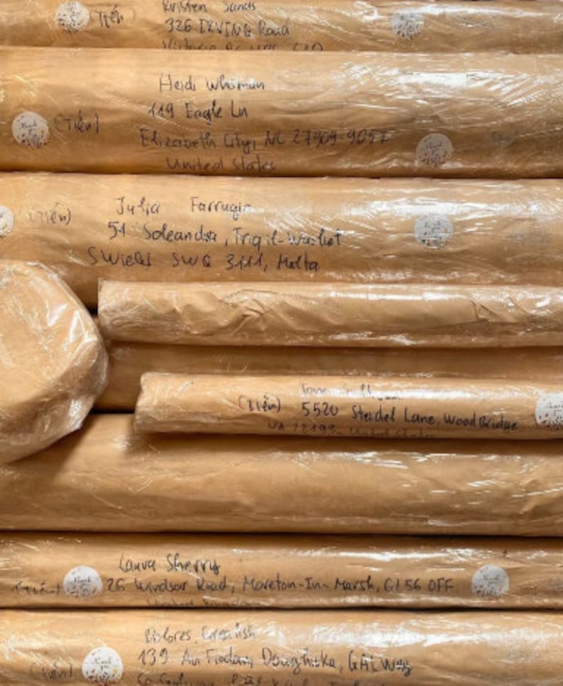 May include: A stack of rolled packages wrapped in brown paper and clear plastic. Handwritten addresses are visible on the paper, with names and street addresses. Small white stickers with handwritten text are also present.