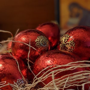 May include: A group of red Christmas ornaments with gold accents are nestled in a bed of shredded paper.