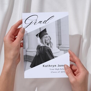 May include: A rectangular graduation announcement card featuring a black and white photograph of a graduate in a cap and gown. The card includes the word Grad in script font at the top and the text Kathryn Jones, Your High School, Class of 20X.