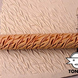 Könnte beinhalten: Ein Holz-Nudelholz mit einem geschnitzten Blattdesign. Das Nudelholz wird verwendet, um ein strukturiertes Muster auf Ton oder Teig zu erstellen. Das Muster ist auf der Oberfläche des Tons im Hintergrund sichtbar.