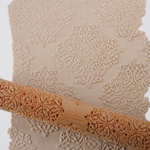 May include: A wooden rolling pin with a detailed carved design. The rolling pin is used to create decorative patterns in dough or fondant.