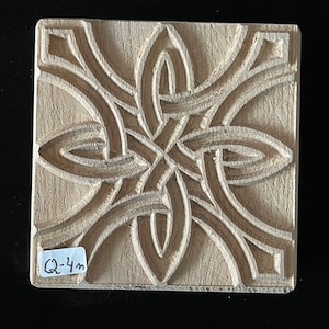 May include: Square wooden stamp with a carved Celtic knot design. The stamp is light brown and features a repeating pattern of interwoven lines and shapes. The text "Q-4m" is visible on a small label.