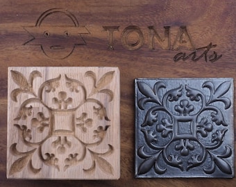 May include: Two square tiles with a decorative floral design. The tile on the left is made of light wood and the tile on the right is made of dark metal.