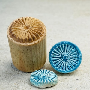 Könnte beinhalten: Drei Ausstecher aus Holz und Keramik in Form einer Blume. Der Holzausstecher ist braun und hat ein erhabenes Design. Die Keramikausstecher sind blau und weiß.