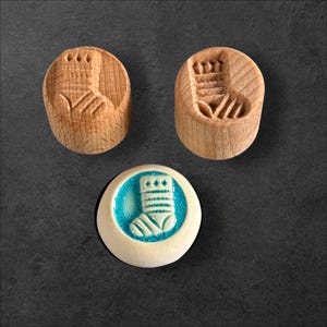 May include: Three Christmas stocking stamps. Two are made of light-coloured wood, each with a carved stocking design. The third stamp has a white ceramic base with a turquoise centre and a stocking design.