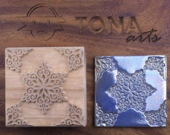 May include: A wooden block with a carved snowflake design is shown next to a blue ceramic tile with the same design. The tile has a metallic sheen. The text "TONA arts" is carved into the wooden surface.