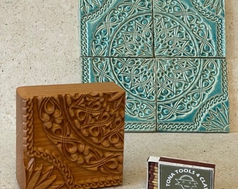 May include: A wooden stamp with a carved design of a Celtic knot. The stamp is next to a set of four teal blue ceramic tiles with a similar design. A box of matches with the text "TONA TOOLS & CLAY" is in the foreground.