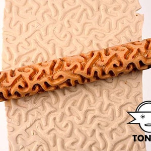 Könnte beinhalten: Ein Holz-Nudelholz mit einem geschnitzten Muster aus abstrakten Formen. Das Nudelholz wird verwendet, um ein strukturiertes Design in Ton oder Teig zu erstellen.