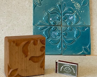 May include: A wooden carving tool with a detailed floral design, next to a set of four turquoise ceramic tiles with a similar floral pattern. A matchbox with the text "TONA TOOLS & CLAY" is also visible.