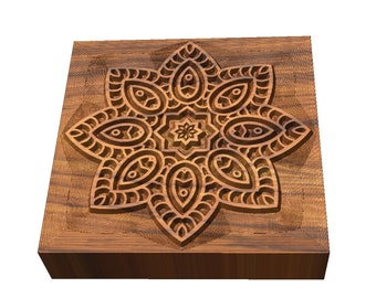 May include: A square wooden block with a carved mandala design in the centre. The mandala is intricate and detailed, with a brown colour.