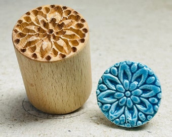 May include: Two round wooden stamps with carved floral designs. One stamp is light brown wood with a natural wood finish and the other is a blue ceramic stamp.