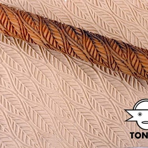 Könnte beinhalten: Ein Holz-Nudelholz mit einem geschnitzten Blatt-Muster. Das Nudelholz wird verwendet, um ein geprägtes Muster auf Ton oder Teig zu erstellen. Das Nudelholz wird auf einer Oberfläche mit dem geprägten Muster gezeigt.