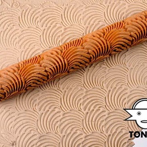 Könnte beinhalten: Ein Nudelholz aus Holz mit einem geschnitzten Muster aus sich überlappenden Wellen. Das Nudelholz wird verwendet, um eine dekorative Textur auf Teig oder Ton zu erzeugen.