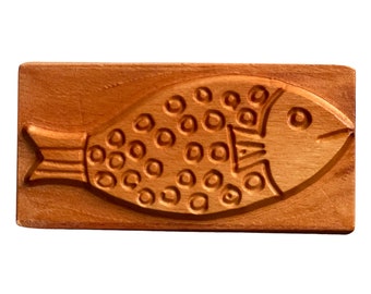 May include: A wooden cookie cutter shaped like a fish with a dotted pattern. The cutter is made of light brown wood and has a smooth surface.