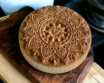 May include: A wooden carving with a detailed mandala design. The carving is circular and has a brown color.