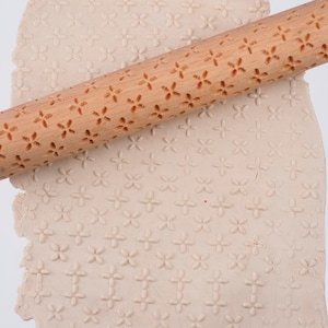 Könnte beinhalten: Ein Nudelholz aus Holz mit einem geprägten Blumenmuster auf der Oberfläche. Das Nudelholz wird verwendet, um ein dekoratives Muster auf Teig zu erstellen.