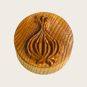 Könnte beinhalten: Ein runder, aus Holz gefertigter Ausstecher in Form einer Zwiebel. Der Ausstecher hat ein detailliertes Design einer Zwiebel mit Stiel.