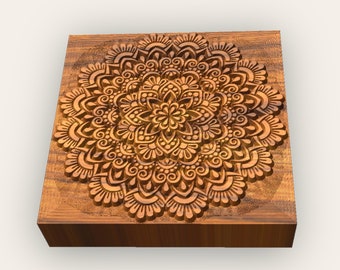 May include: A wooden square block with a carved mandala design. The mandala is intricate and detailed, with a variety of shapes and patterns. The wood is a rich brown color.