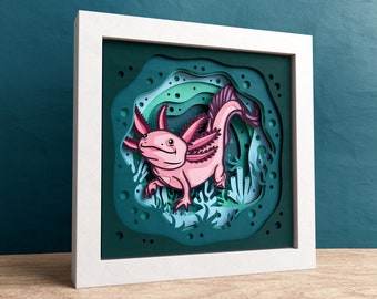 May include: A pink axolotl with feathery gills and a long tail is depicted in a paper cut-out art piece. The axolotl is surrounded by green and blue paper cut-out seaweed and bubbles.