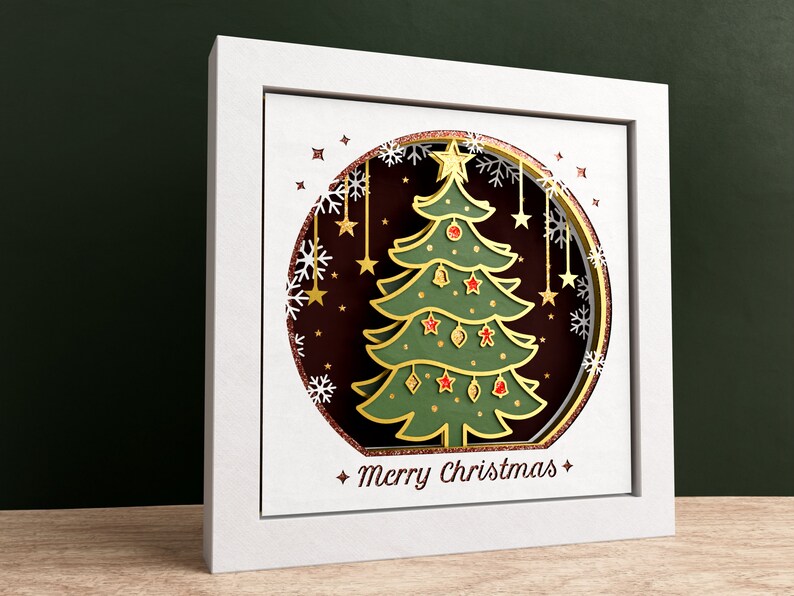 K&ouml;nnte beinhalten: Ein wei&szlig;er Rahmen mit einer goldenen und gr&uuml;nen Papierschnitt-Weihnachtsbaum-Darstellung in einem Kreis mit Schneeflocken und Sternen. Der Text "Merry Christmas" befindet sich am unteren Rand des Rahmens.