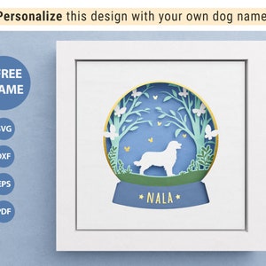 Peut inclure: Une silhouette blanche d'un chien à l'intérieur d'un globe à neige en papier découpé bleu et vert avec le nom "NALA" écrit en dessous. Le globe à neige est dans un cadre blanc.