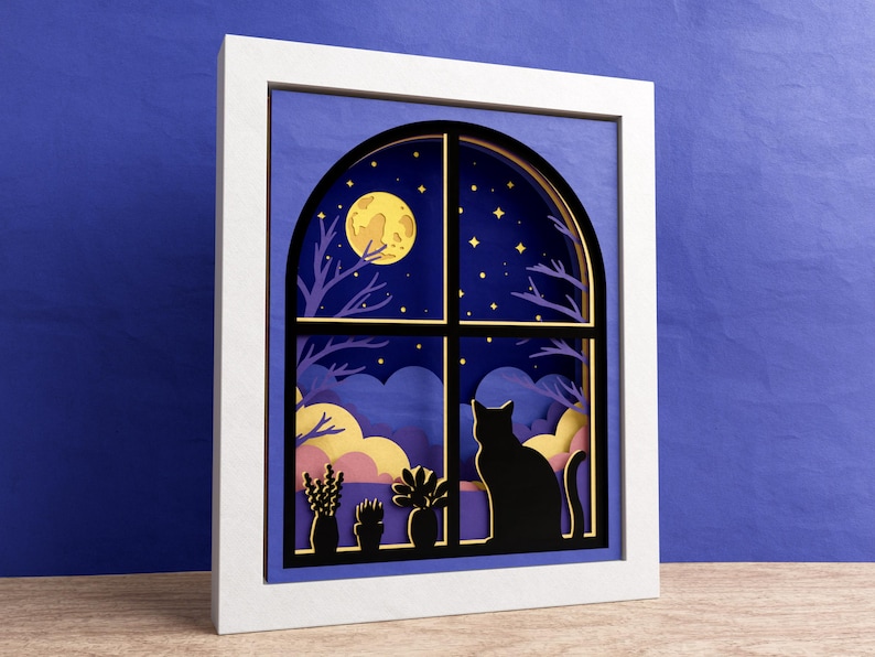 May include: A white frame with a blue background and a black window with a cat silhouette looking out at a yellow moon and stars. The window is arched and has a layered paper design.