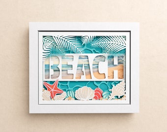May include: White frame with a paper cut-out design of a beach scene. The design includes palm leaves, seashells, a starfish, and the word "BEACH" with a beach scene visible through the cut-out letters.
