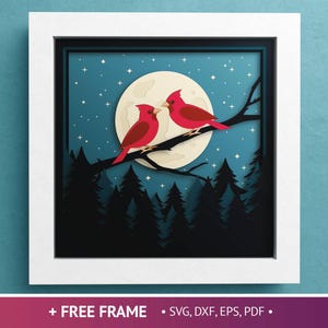 May include: A framed paper art piece depicting two red cardinals on a branch, set against a full moon and a starry night sky. The artwork includes silhouetted trees. The frame is white.