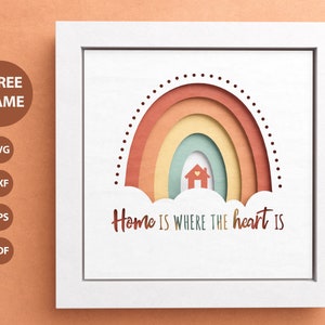 May include: A white frame with a white background and a rainbow with a house in the middle. The rainbow is made of paper and has a layered effect. The text "Home is where the heart is" is written below the rainbow.