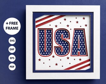 Può includere: Una cornice bianca con un bordo interno blu circonda un design di carta tagliata in rosso, bianco e blu della parola "USA". Le lettere sono riempite con un motivo di stelle bianche su sfondo blu. Lo sfondo del design è un motivo a strisce rosse e bianche.
