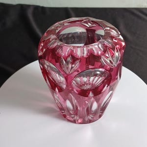 May include: A deep magenta glass vase featuring a cut crystal design with clear, circular, and petal-shaped facets. The heavy glass vessel has a wide, open top and a tapered body, showcasing a vibrant pink hue that transitions to clear glass.