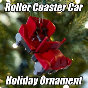 May include: A red roller coaster car holiday ornament. The ornament is suspended against a backdrop of a Christmas tree with lights. The text "Roller Coaster Car" and "Holiday Ornament" are displayed.