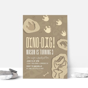 May include: A tan and brown invitation card with a dinosaur skeleton and footprints. The text reads "Dino-Dig! Mason is turning 3. Join us for a fossilized time. June 15 at 3PM. 12345 T-Rex Drive, Jurassic CA. RSVP to Michelle by June 5 at 619.123.4567."
