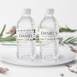 May include: Two clear plastic water bottles with personalized labels. The labels feature a gray and orange tool theme with the text "Happy Birthday Daniel" and "Daniel's Third Birthday".