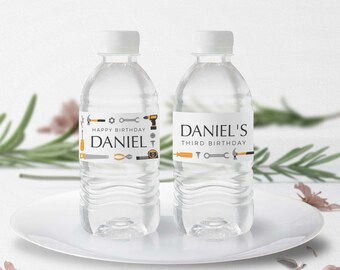 May include: Two clear plastic water bottles with personalized labels. The labels feature a gray and orange tool theme with the text "Happy Birthday Daniel" and "Daniel's Third Birthday".