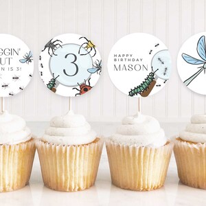 Peut inclure: Quatre décorations de cupcakes sur le thème des insectes. Les décorations représentent une loupe avec des insectes, une libellule, le chiffre 3 et le texte "Buggin' Out Mason is 3!"