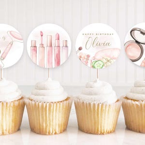 May include: Four cupcakes with white icing, each with a circular decoration. The decorations show makeup illustrations and the text "Olivia is 8" and "Happy Birthday Olivia".