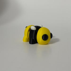 May include: A small, black and yellow bee figurine with white accents. The bee is made of plastic and has a cartoonish appearance.