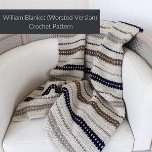 May include: A crocheted blanket featuring horizontal stripes in cream, dark navy blue, and light brown. The text "William Blanket (Worsted Version) Crochet Pattern" is overlaid on the image. The blanket has a textured stitch pattern throughout.