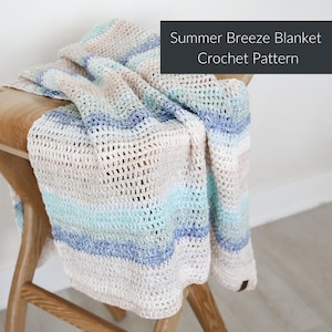 Può includere: Una coperta all'uncinetto nei toni del crema, blu e verde acqua è drappeggiata su uno sgabello di legno. La coperta presenta strisce orizzontali e il testo "Summer Breeze Blanket Crochet Pattern" in un riquadro grigio scuro.