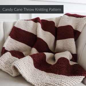 Puede incluir: Una manta tejida con anchas rayas horizontales que alternan colores burdeos intenso y crema. El texto Candy Cane Throw Knitting Pattern aparece en un recuadro gris oscuro en la parte superior de la imagen, indicando el tipo de artículo.