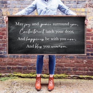 May include: A black chalkboard sign with white text that reads: "May joy and peace surround you, Contentment latch your door, And happiness be with you now, And bless you evermore."