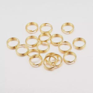 May include: A selection of gold-coloured split key rings, arranged on a white surface. The key rings are circular with a split opening, suitable for attaching keys or small objects. The rings are made of a shiny metal.