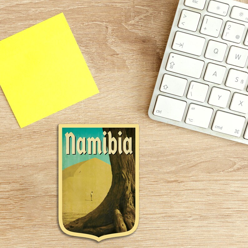 K&ouml;nnte beinhalten: Ein Reiseaufkleber im Vintage-Stil mit einem Farbschema in Gelb, Braun und Blau. Der Aufkleber zeigt eine W&uuml;stenlandschaft mit einem gro&szlig;en Baum und dem Wort "Namibia" in einer fetten, stilisierten Schrift.