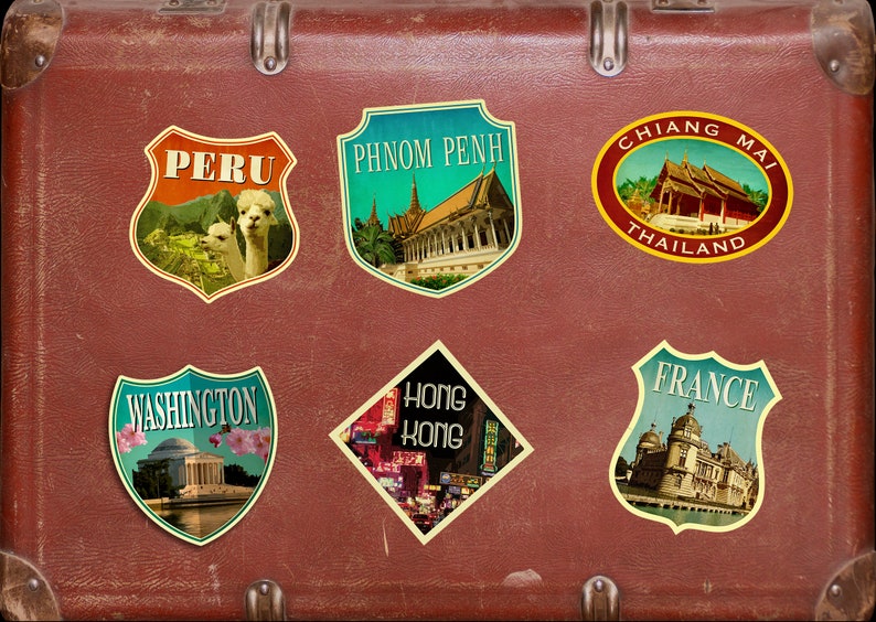 May include: A vintage suitcase covered in travel stickers. The stickers feature destinations like Peru, Phnom Penh, Chiang Mai, Thailand, Washington, Hong Kong, and France.