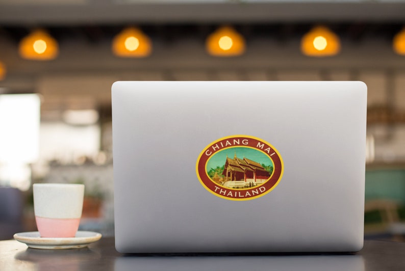 May include: A laptop computer with a sticker of a red building with a yellow roof and the text "CHIANG MAI THAILAND" in a circle.