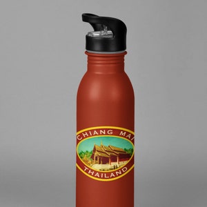May include: A red stainless steel water bottle with a black lid and a white oval sticker that says "Chiang Mai Thailand" with a picture of a building in the center.