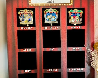 May include: A wooden shadowbox with a red curtain design, featuring the text "MAGICAL THEATER NOW SHOWING 2026." It has spaces for pins, labeled with months from January to December. The word "SAMPLE" is at the bottom.